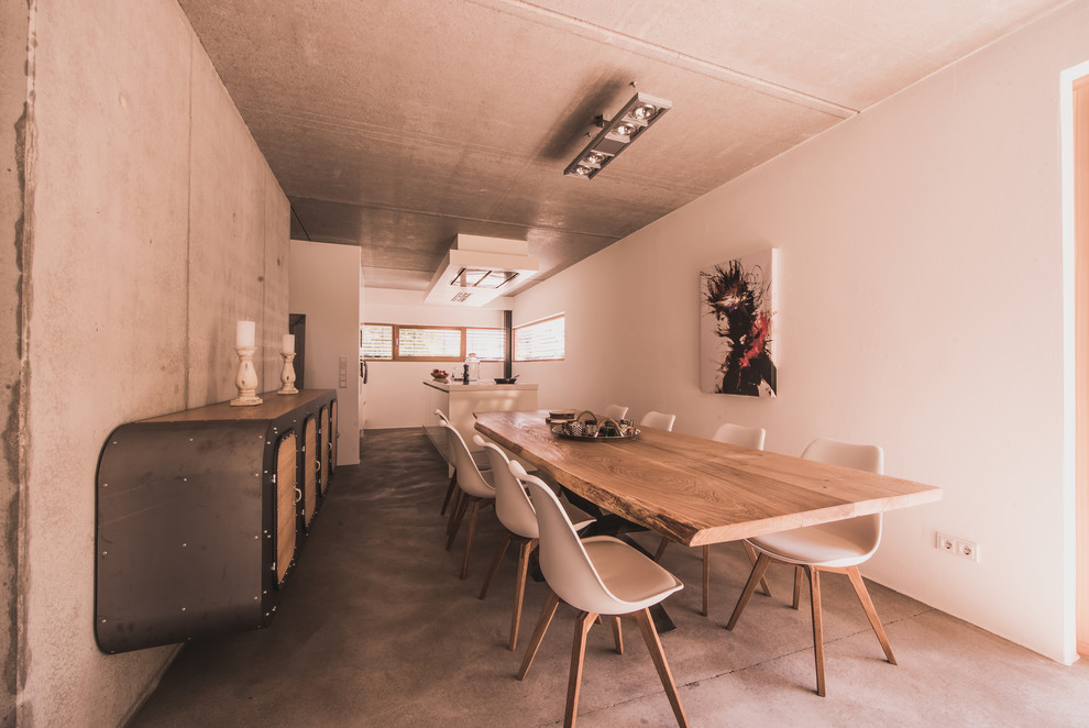Réalisation d'une très grande salle à manger ouverte sur le salon urbaine avec un mur gris, sol en béton ciré, une cheminée standard et un manteau de cheminée en béton.