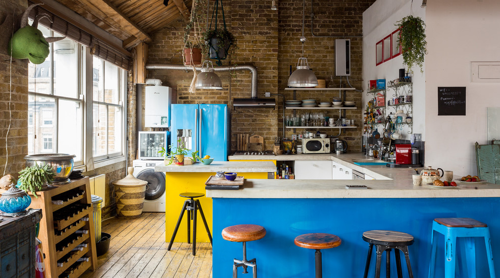 Photo of an eclectic u-shaped kitchen in London with flat-panel cabinets, yellow cabinets, brick splashback, coloured appliances, light hardwood floors, multiple islands, beige floor and beige benchtop.