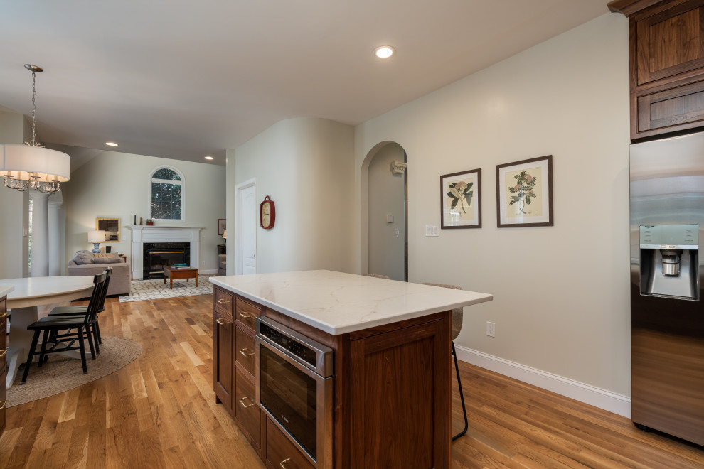Example of a mid-sized transitional u-shaped medium tone wood floor eat-in kitchen design with a farmhouse sink, beaded inset cabinets, medium tone wood cabinets, white backsplash, stainless steel appliances and an island