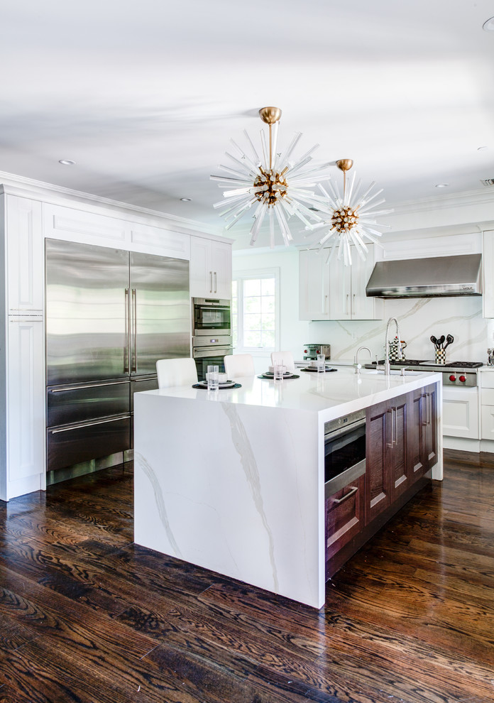 Inspiration for a large transitional galley dark wood floor and brown floor open concept kitchen remodel in New York with a drop-in sink, shaker cabinets, white cabinets, quartzite countertops, white backsplash, stone slab backsplash, stainless steel appliances and an island