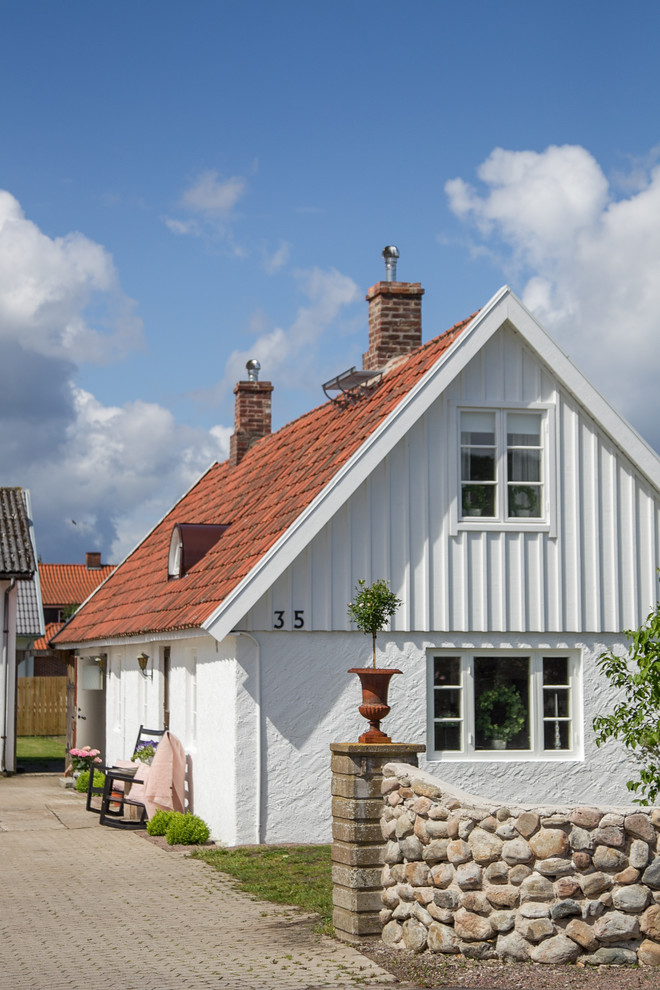 This is an example of a small country two-storey white house exterior in Malmo with mixed siding, a gable roof and a tile roof.