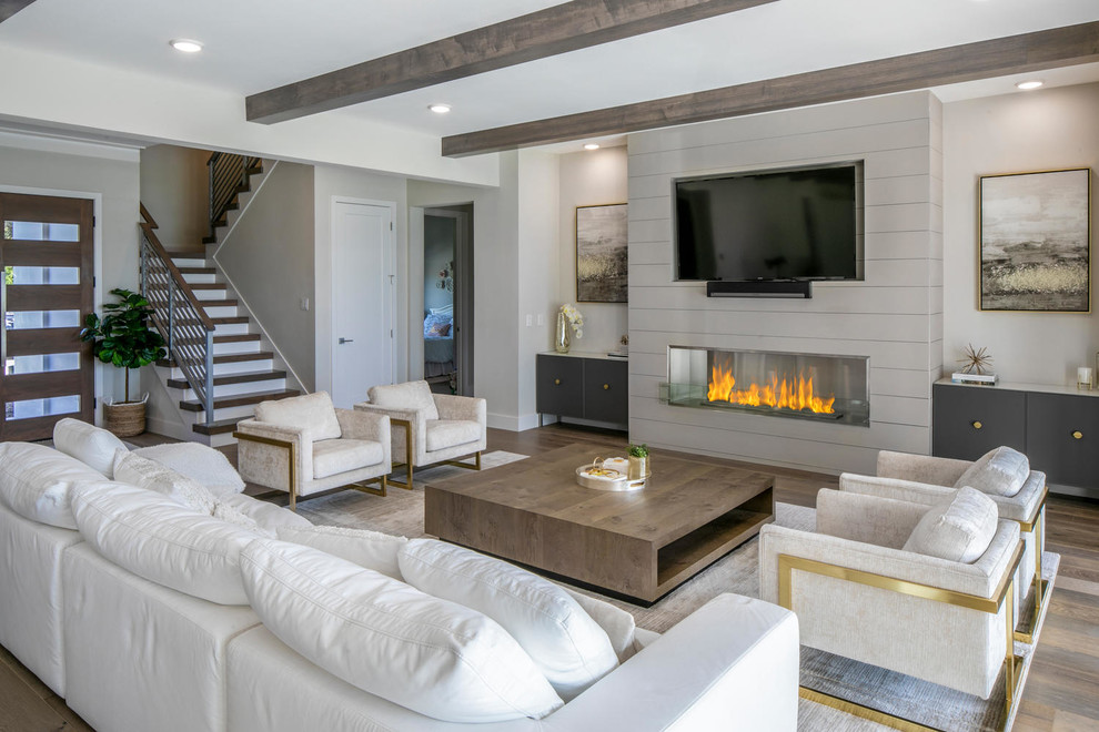 Inspiration for an expansive modern open concept living room in Tampa with white walls, medium hardwood floors, a wood fireplace surround, a wall-mounted tv, brown floor and a ribbon fireplace.