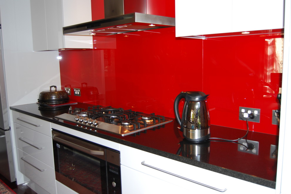This is an example of a mid-sized contemporary l-shaped eat-in kitchen in Sydney with an undermount sink, flat-panel cabinets, white cabinets, red splashback, glass sheet splashback, stainless steel appliances, dark hardwood floors and with island.