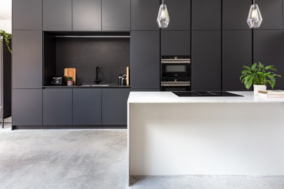 Mid-sized contemporary galley eat-in kitchen in London with a single-bowl sink, recessed-panel cabinets, black cabinets, marble benchtops, black splashback, slate splashback, black appliances, concrete floors, with island, grey floor and white benchtop.