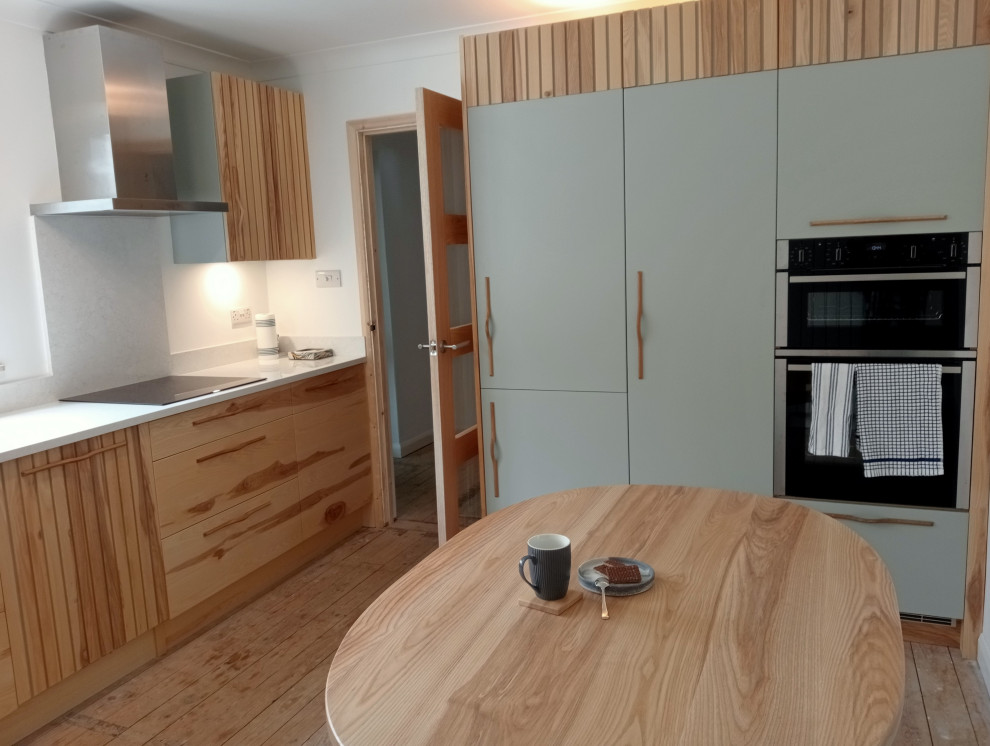 Medium sized contemporary l-shaped kitchen/diner in Cornwall with a double-bowl sink, flat-panel cabinets, light wood cabinets, engineered stone countertops, white splashback, engineered quartz splashback, stainless steel appliances, light hardwood flooring, no island and white worktops.