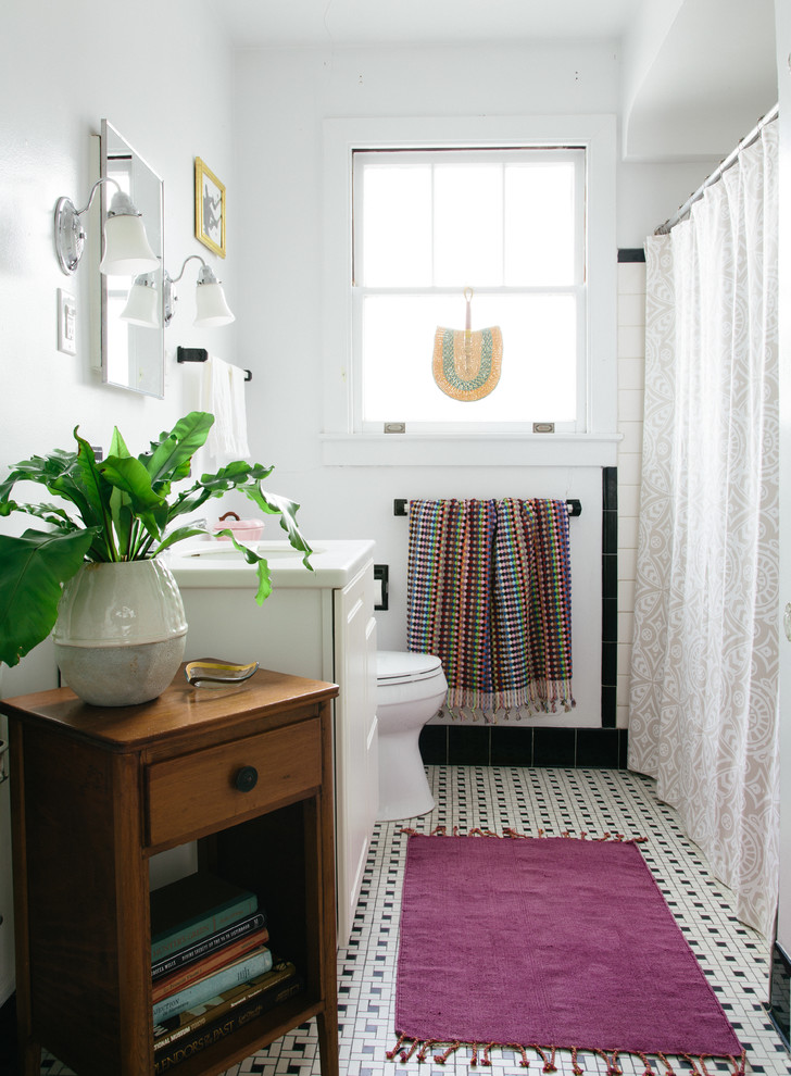 This is an example of a mid-sized eclectic 3/4 bathroom in New Orleans with a shower/bathtub combo, white cabinets, black tile, black and white tile, white tile, porcelain tile, white walls, porcelain floors, an undermount sink, solid surface benchtops, multi-coloured floor and white benchtops.