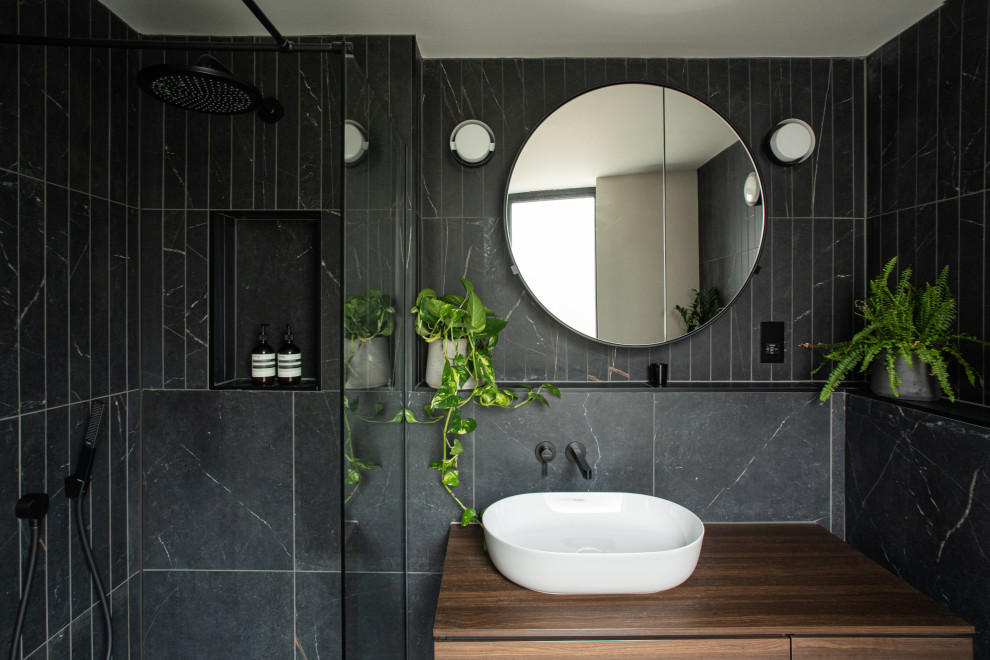 This is an example of a small scandinavian master bathroom in London with flat-panel cabinets, brown cabinets, a corner shower, black tile, porcelain tile, black walls, porcelain floors, wood benchtops, black floor, brown benchtops, a niche, a single vanity, a floating vanity, a vessel sink and an open shower.