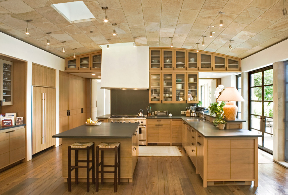 Photo of a transitional u-shaped kitchen in Seattle with an undermount sink, glass-front cabinets, medium wood cabinets, panelled appliances, dark hardwood floors, with island and black splashback.