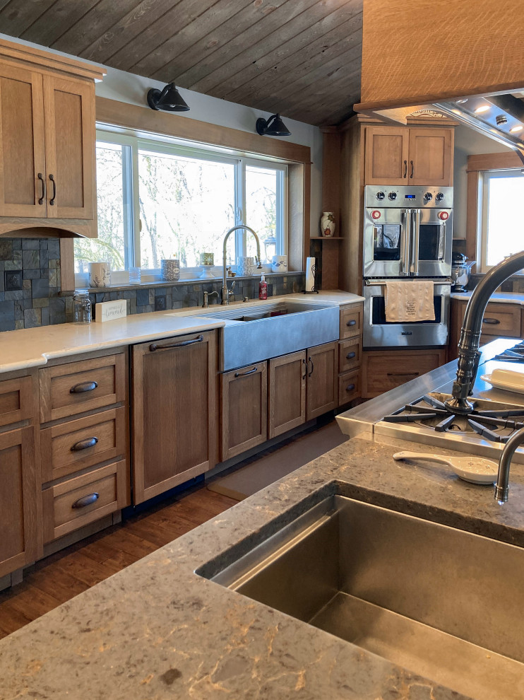 Inspiration for a large arts and crafts galley eat-in kitchen in Chicago with a farmhouse sink, shaker cabinets, medium wood cabinets, multi-coloured splashback, stone tile splashback, stainless steel appliances, medium hardwood floors, with island, brown floor, grey benchtop and timber.