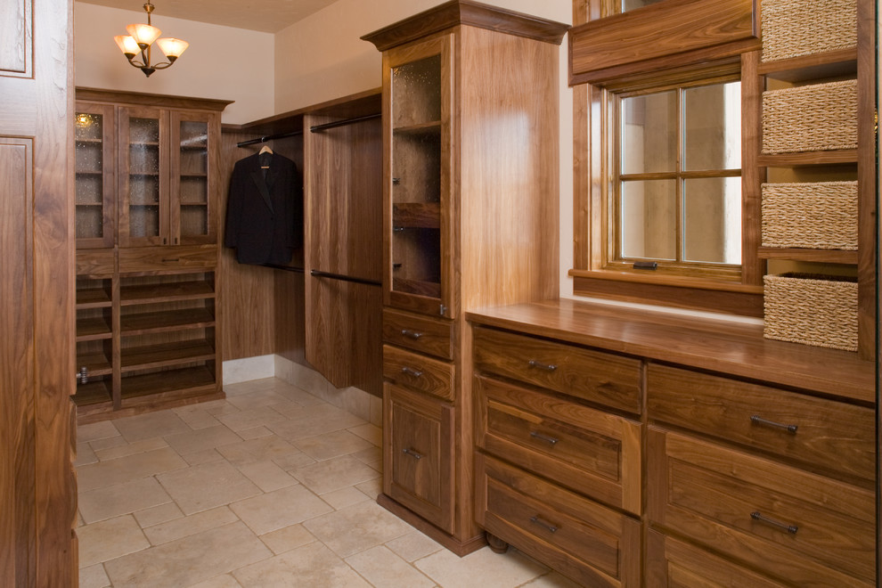 Inspiration for a large mediterranean gender-neutral walk-in wardrobe in Portland with recessed-panel cabinets, dark wood cabinets and travertine floors.