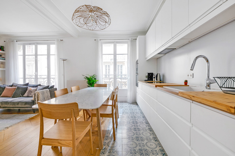 This is an example of a large scandinavian single-wall open plan kitchen in Paris with a drop-in sink, white cabinets, wood benchtops, white splashback, metal splashback, cement tiles, no island, flat-panel cabinets, grey floor and brown benchtop.
