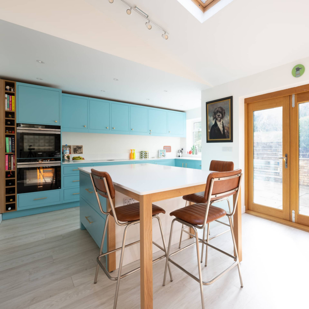 Идея дизайна: угловая кухня среднего размера в стиле модернизм с обеденным столом, накладной мойкой, плоскими фасадами, синими фасадами, столешницей из кварцита, белым фартуком, черной техникой и островом