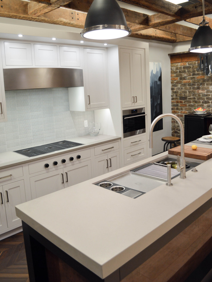 Mid-sized transitional galley kitchen in Cleveland with an undermount sink, shaker cabinets, white cabinets, quartz benchtops, grey splashback, porcelain splashback, stainless steel appliances, medium hardwood floors, with island, brown floor and white benchtop.