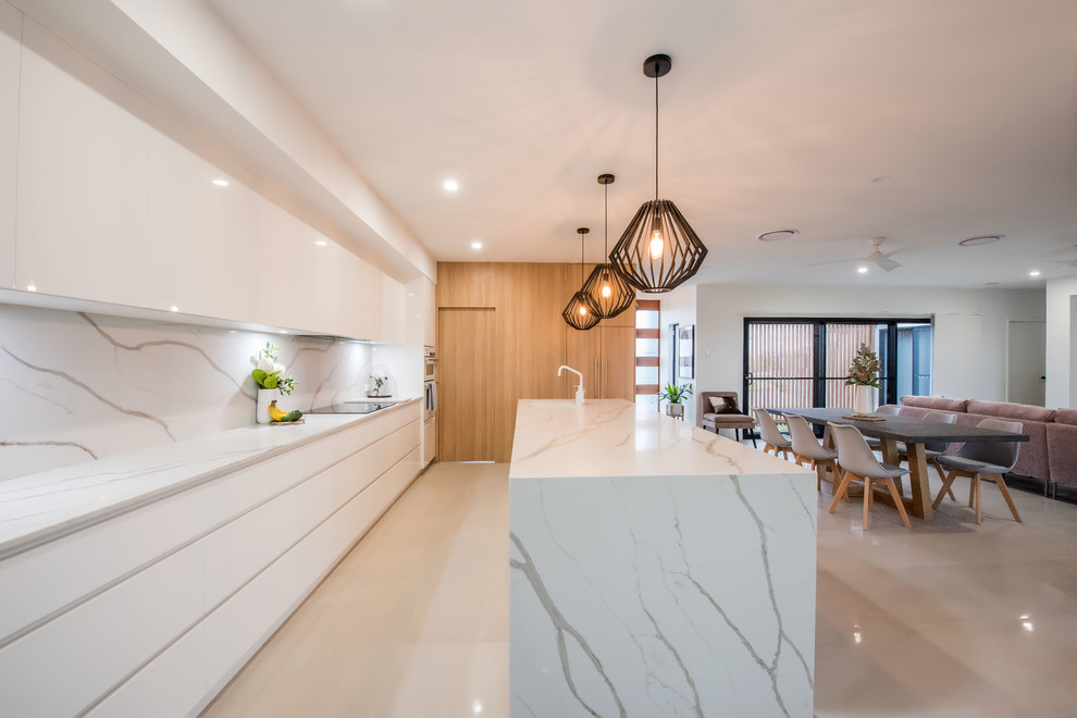 Inspiration for a large contemporary galley open plan kitchen in Other with an undermount sink, flat-panel cabinets, light wood cabinets, marble benchtops, white splashback, marble splashback, white appliances, ceramic floors, with island, white floor and white benchtop.