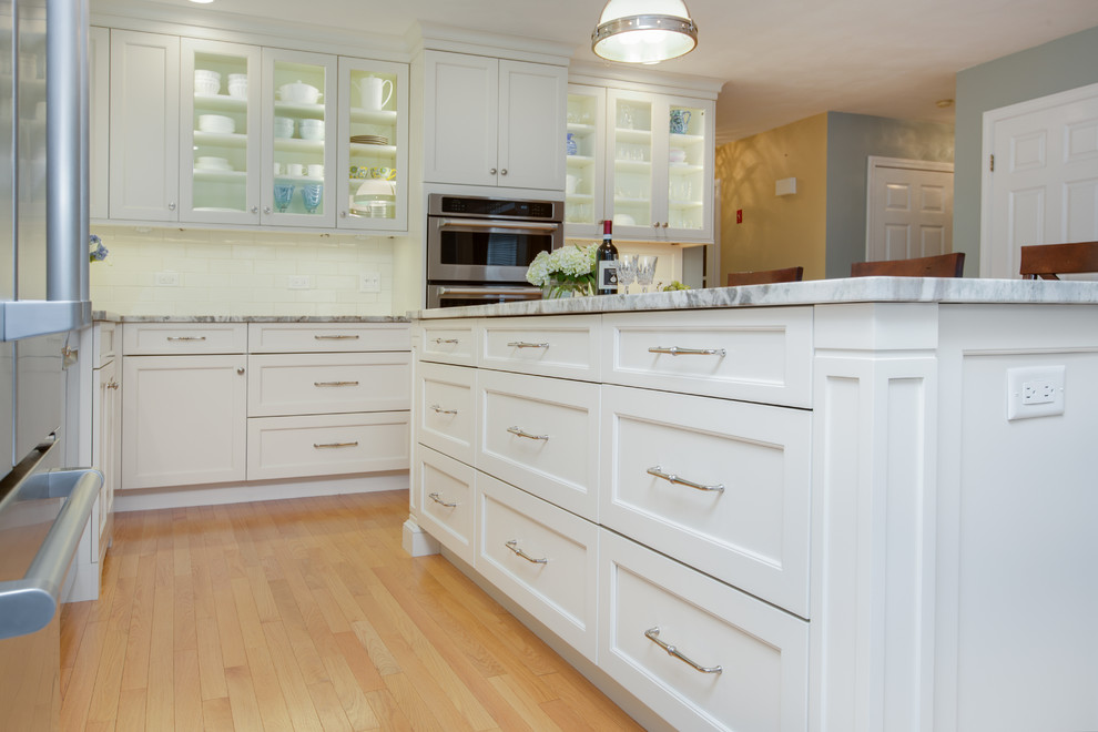 Example of a transitional l-shaped light wood floor eat-in kitchen design in Boston with an undermount sink, recessed-panel cabinets, white cabinets, quartzite countertops, white backsplash, subway tile backsplash, stainless steel appliances and an island