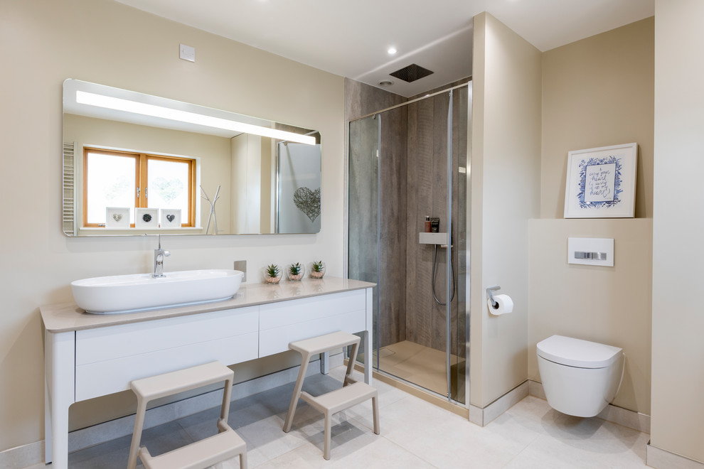 Photo of a mid-sized beach style kids bathroom in West Midlands with white cabinets, a corner shower, a wall-mount toilet, beige walls, porcelain floors, a vessel sink, quartzite benchtops, a hinged shower door, beige benchtops, flat-panel cabinets and white floor.