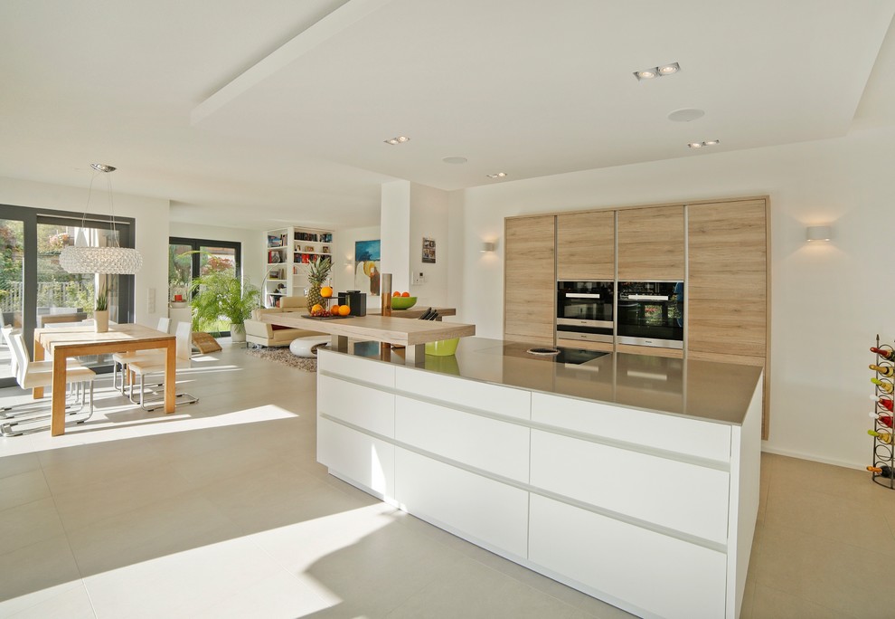 This is an example of a large contemporary single-wall eat-in kitchen in Munich with flat-panel cabinets, white cabinets, black appliances, with island, beige floor, grey benchtop, a drop-in sink, beige splashback, timber splashback and concrete floors.