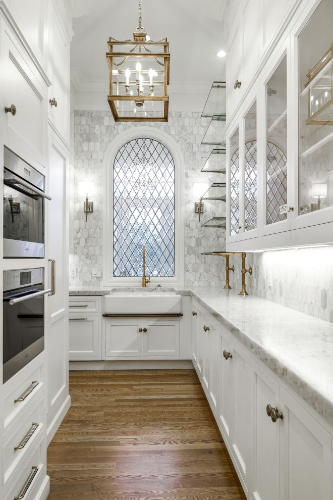 This is an example of an expansive u-shaped kitchen pantry in Salt Lake City with a farmhouse sink, raised-panel cabinets, white cabinets, marble benchtops, grey splashback, marble splashback, panelled appliances, medium hardwood floors, multiple islands, brown floor and white benchtop.