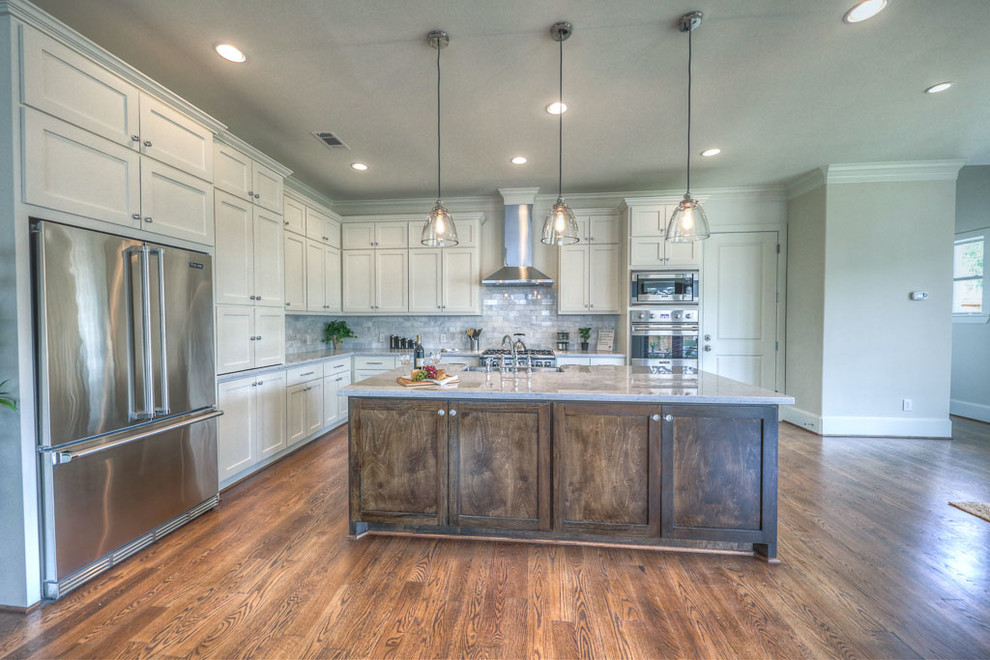 Example of a mid-sized transitional l-shaped medium tone wood floor and brown floor open concept kitchen design in Houston with a farmhouse sink, shaker cabinets, white cabinets, marble countertops, gray backsplash, marble backsplash, stainless steel appliances, an island and gray countertops