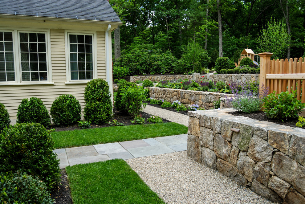 This is an example of a mid-sized traditional sloped garden in Boston with a retaining wall.