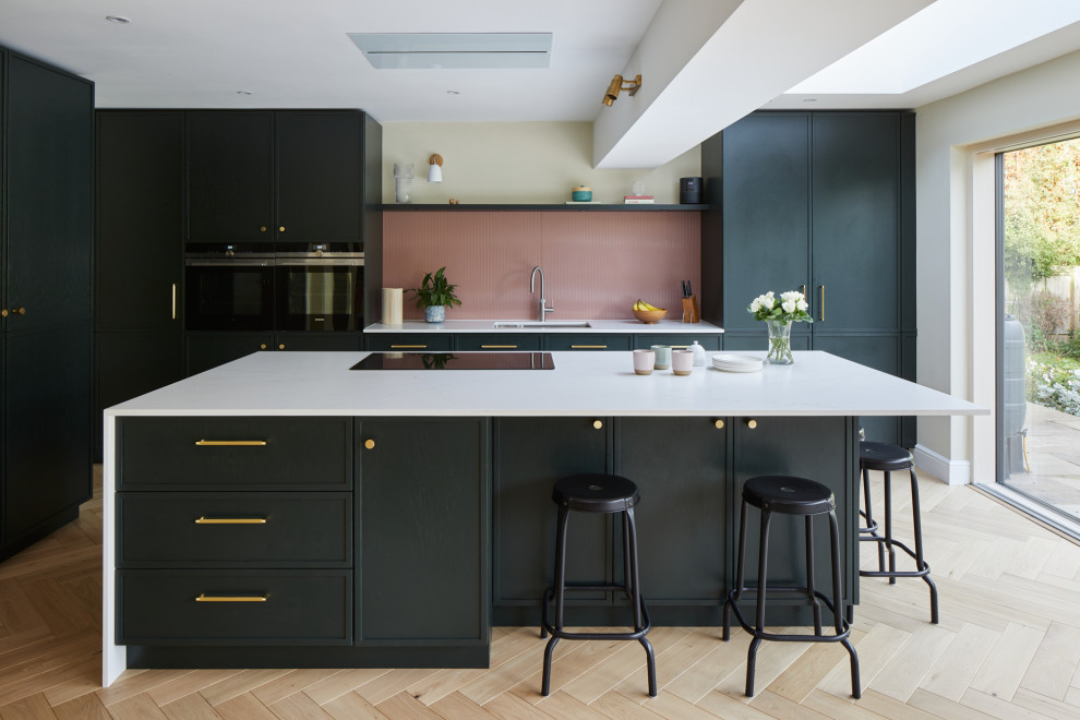Design ideas for a large contemporary l-shaped kitchen/diner in Kent with recessed-panel cabinets, green cabinets, engineered stone countertops, pink splashback, glass sheet splashback, stainless steel appliances, an island and white worktops.