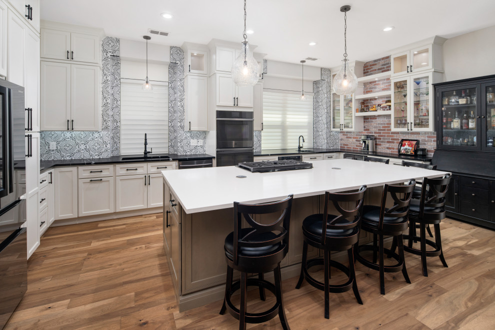 Inspiration for a large traditional u-shaped kitchen/diner in Dallas with a submerged sink, glass-front cabinets, white cabinets, engineered stone countertops, blue splashback, brick splashback, black appliances, an island and black worktops.