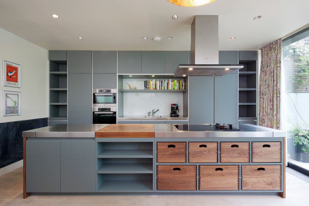 This is an example of a large contemporary kitchen in London with an integrated sink, flat-panel cabinets, grey cabinets, stainless steel benchtops, white splashback, glass sheet splashback, stainless steel appliances and with island.