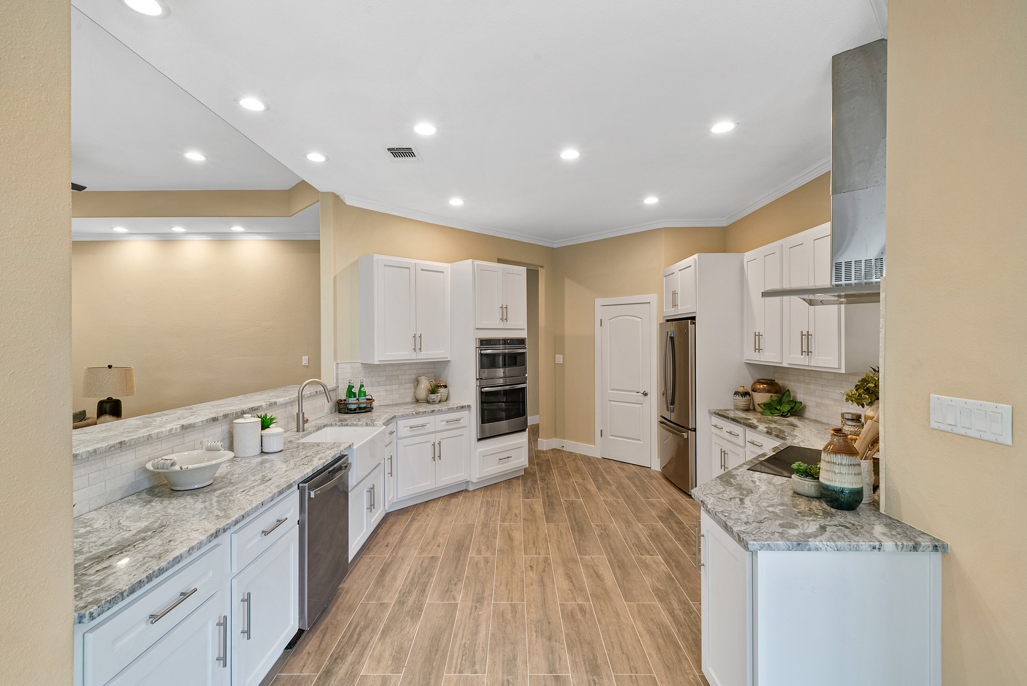 Mid-sized trendy l-shaped porcelain tile and brown floor eat-in kitchen photo in Orange County with a farmhouse sink, shaker cabinets, white cabinets, granite countertops, ceramic backsplash, stainles