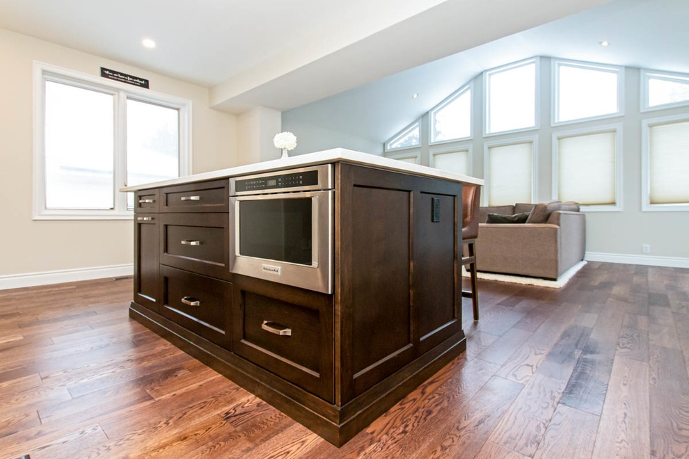 Inspiration for a mid-sized transitional l-shaped medium tone wood floor and brown floor open concept kitchen remodel with an undermount sink, shaker cabinets, white cabinets, quartzite countertops, white backsplash, stone tile backsplash, stainless steel appliances, an island and white countertops