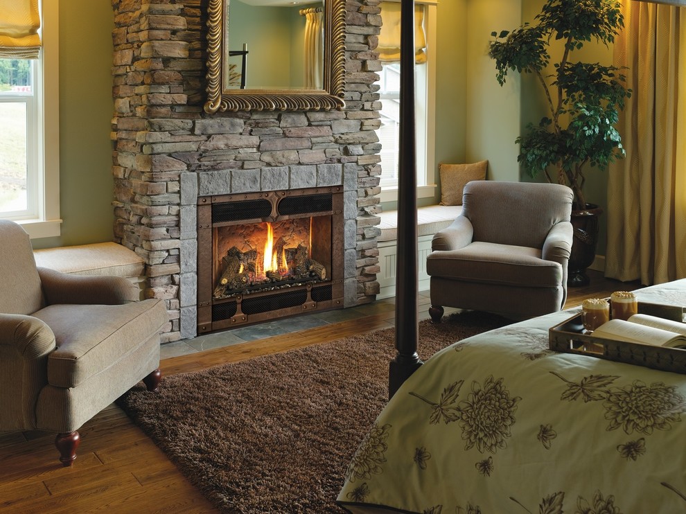 This is an example of a mid-sized traditional bedroom in Other with beige walls, medium hardwood floors, a standard fireplace, a stone fireplace surround and brown floor.