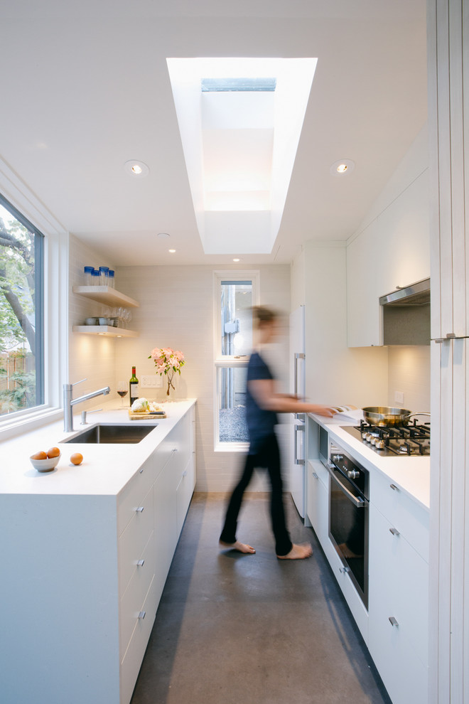 This is an example of a small contemporary galley kitchen in Vancouver with white cabinets, white splashback, concrete floors, white benchtop, an undermount sink, flat-panel cabinets, no island and grey floor.