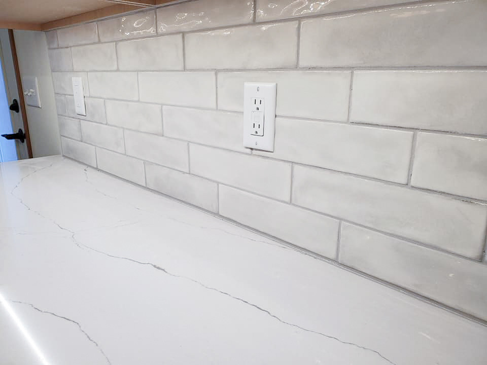 Inspiration for a mid-sized rustic l-shaped vinyl floor, brown floor and vaulted ceiling open concept kitchen remodel with an undermount sink, flat-panel cabinets, medium tone wood cabinets, quartz countertops, white backsplash, ceramic backsplash, stainless steel appliances, an island and white countertops