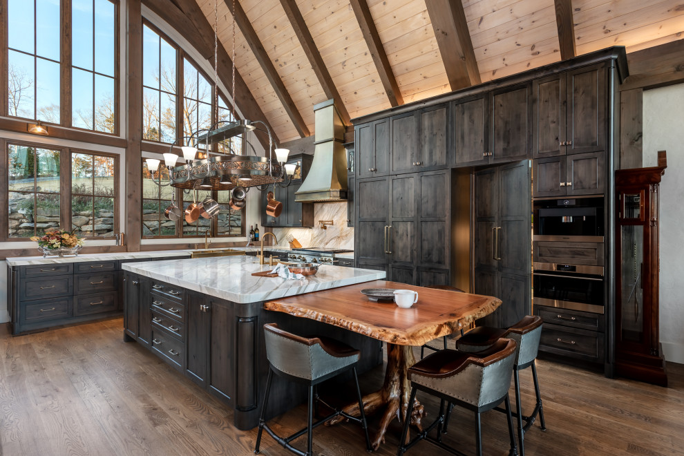 Design ideas for an expansive rustic l-shaped open plan kitchen in Other with a belfast sink, recessed-panel cabinets, dark wood cabinets, composite countertops, white splashback, engineered quartz splashback, integrated appliances, medium hardwood flooring, an island, brown floors, white worktops and exposed beams.