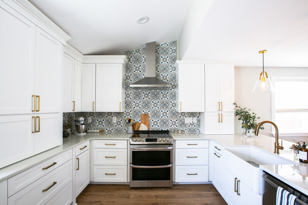 Inspiration for a mid-sized transitional u-shaped eat-in kitchen in Denver with a farmhouse sink, shaker cabinets, white cabinets, quartz benchtops, multi-coloured splashback, cement tile splashback, stainless steel appliances, vinyl floors, a peninsula, brown floor and grey benchtop.