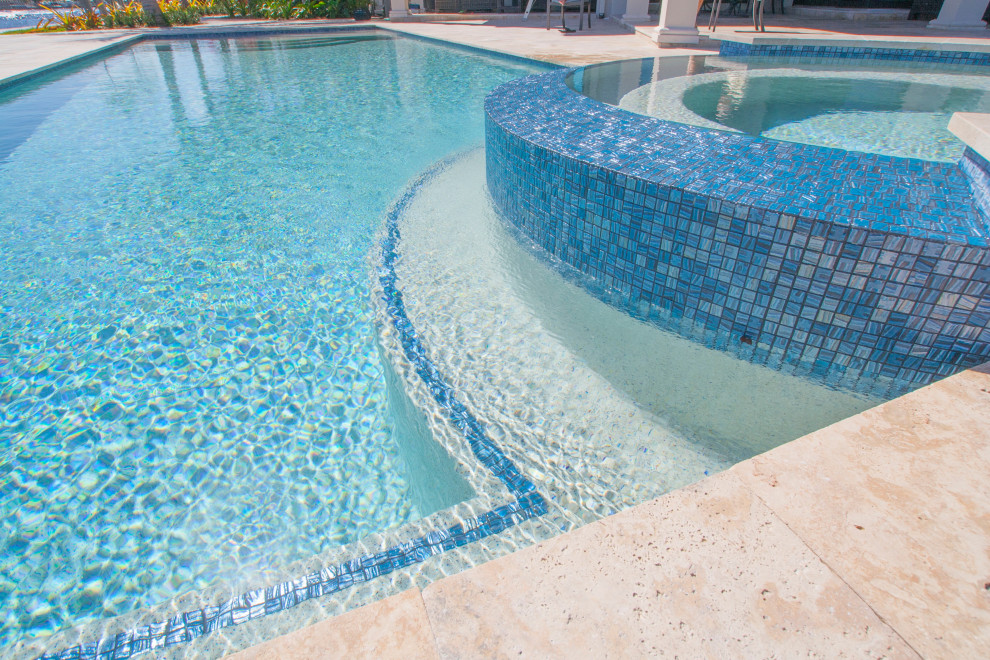 Design ideas for a mid-sized tropical backyard custom-shaped lap pool in Miami with a hot tub and natural stone pavers.