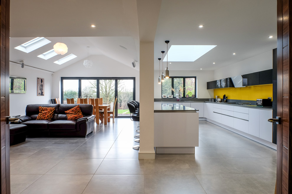 Large modern l-shaped open plan kitchen in Essex with a single-bowl sink, flat-panel cabinets, white cabinets, quartzite benchtops, yellow splashback, glass sheet splashback, black appliances, porcelain floors and with island.