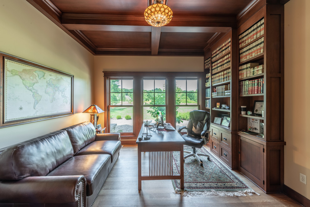 This is an example of a small arts and crafts home office in Milwaukee with a library, beige walls, light hardwood floors, a freestanding desk and yellow floor.