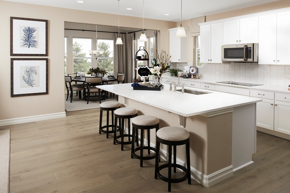 Photo of a contemporary kitchen in Denver with white cabinets, with island, brown floor and white benchtop.