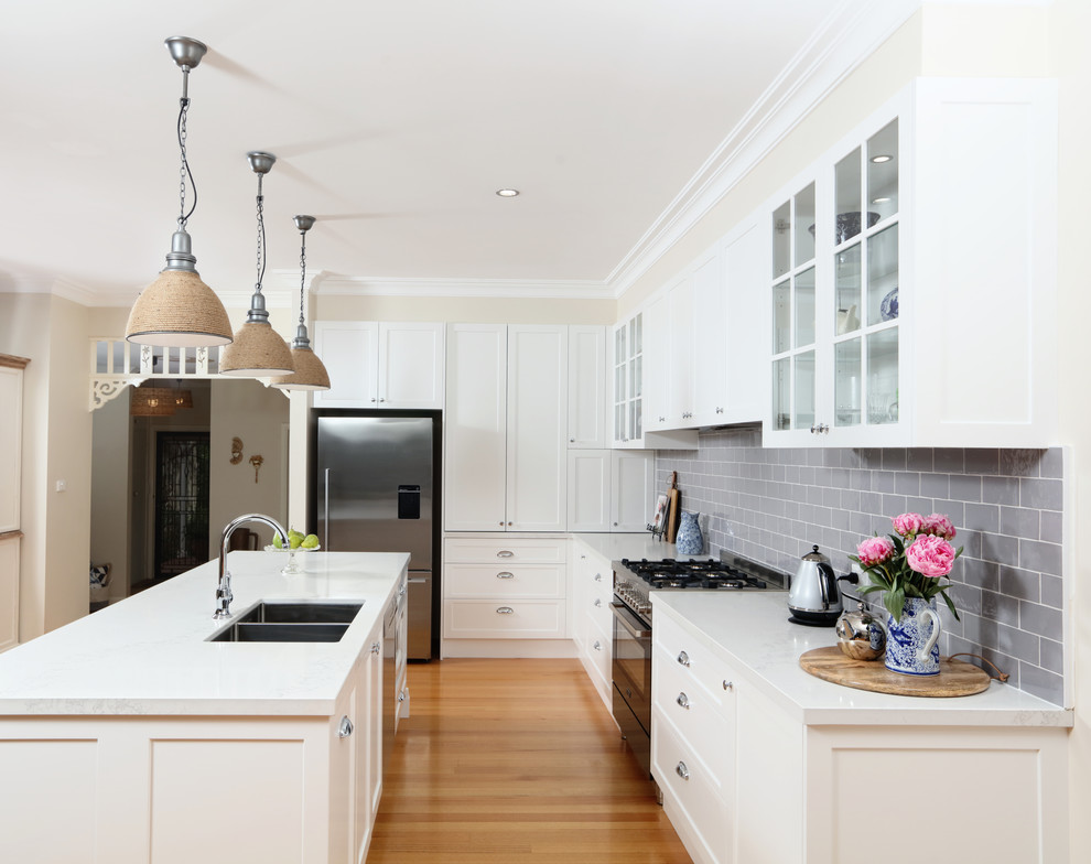 Inspiration for a mid-sized transitional l-shaped eat-in kitchen in Melbourne with an undermount sink, shaker cabinets, white cabinets, quartz benchtops, grey splashback, subway tile splashback, black appliances, medium hardwood floors and with island.