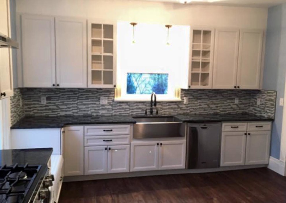 Inspiration for a mid-sized transitional l-shaped medium tone wood floor and brown floor kitchen pantry remodel with a farmhouse sink, recessed-panel cabinets, white cabinets, granite countertops, multicolored backsplash, glass tile backsplash, stainless steel appliances, no island and black countertops