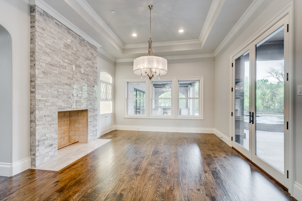 This is an example of a mid-sized transitional dining room in Dallas with white walls, medium hardwood floors, a standard fireplace and a stone fireplace surround.