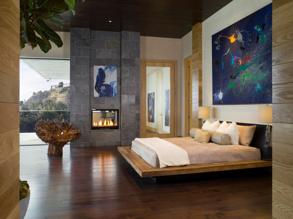 Großes Modernes Hauptschlafzimmer mit weißer Wandfarbe, braunem Holzboden, Kamin, Kaminumrandung aus Stein, braunem Boden, Holzdecke und Holzwänden in Los Angeles