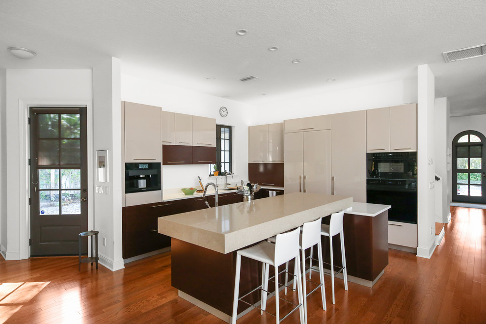 Large contemporary l-shaped open plan kitchen in Other with flat-panel cabinets, beige cabinets, solid surface benchtops, medium hardwood floors, with island, brown floor, white benchtop, an undermount sink and panelled appliances.