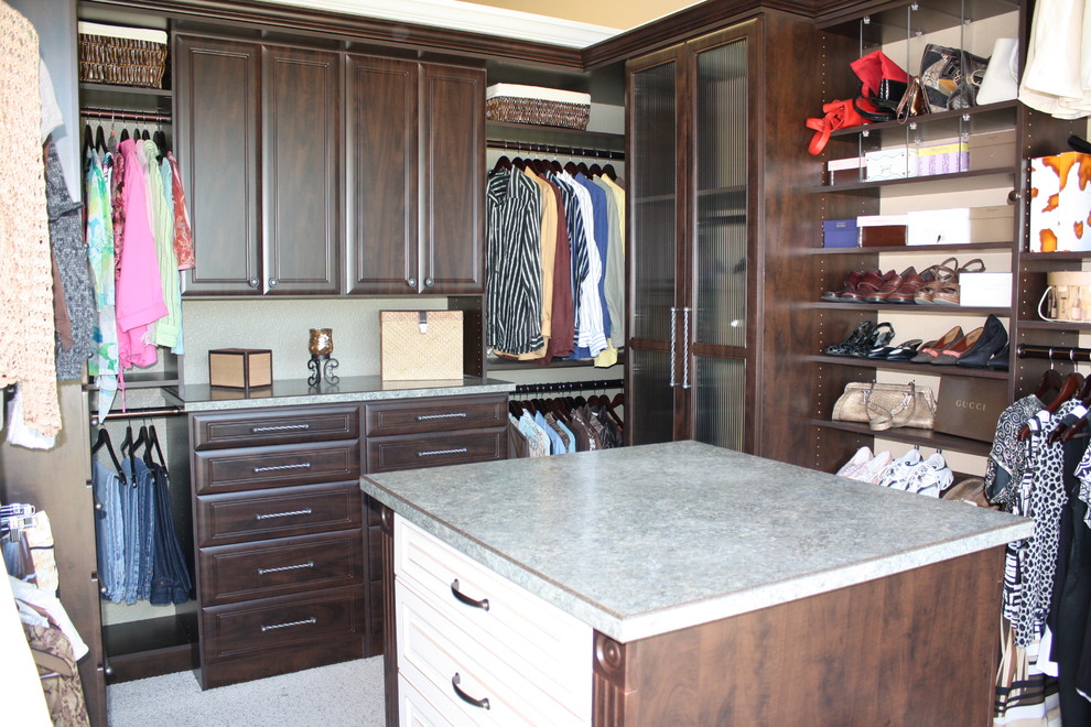 This is an example of a mid-sized gender-neutral walk-in wardrobe in Sacramento with raised-panel cabinets, dark wood cabinets, carpet and grey floor.