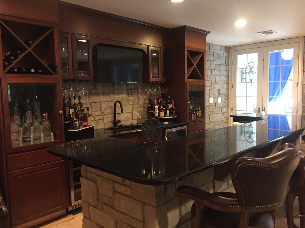 Photo of a mid-sized transitional seated home bar in Philadelphia with an undermount sink, recessed-panel cabinets, medium wood cabinets, granite benchtops, grey splashback, stone tile splashback and travertine floors.
