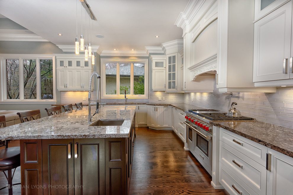 Expansive traditional u-shaped open plan kitchen in Toronto with an undermount sink, recessed-panel cabinets, white cabinets, quartzite benchtops, grey splashback, glass tile splashback, stainless steel appliances, medium hardwood floors and with island.