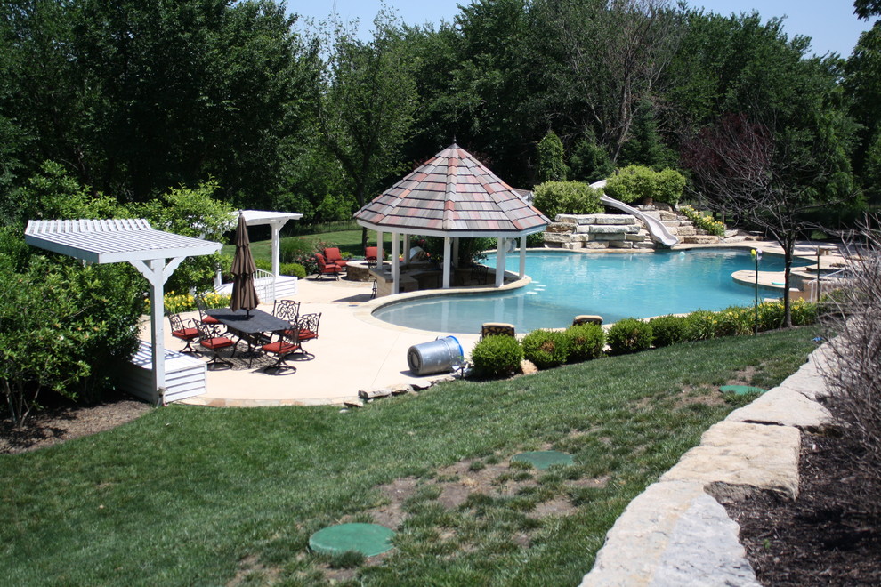 Large transitional backyard custom-shaped natural pool in Other with a water slide and concrete slab.