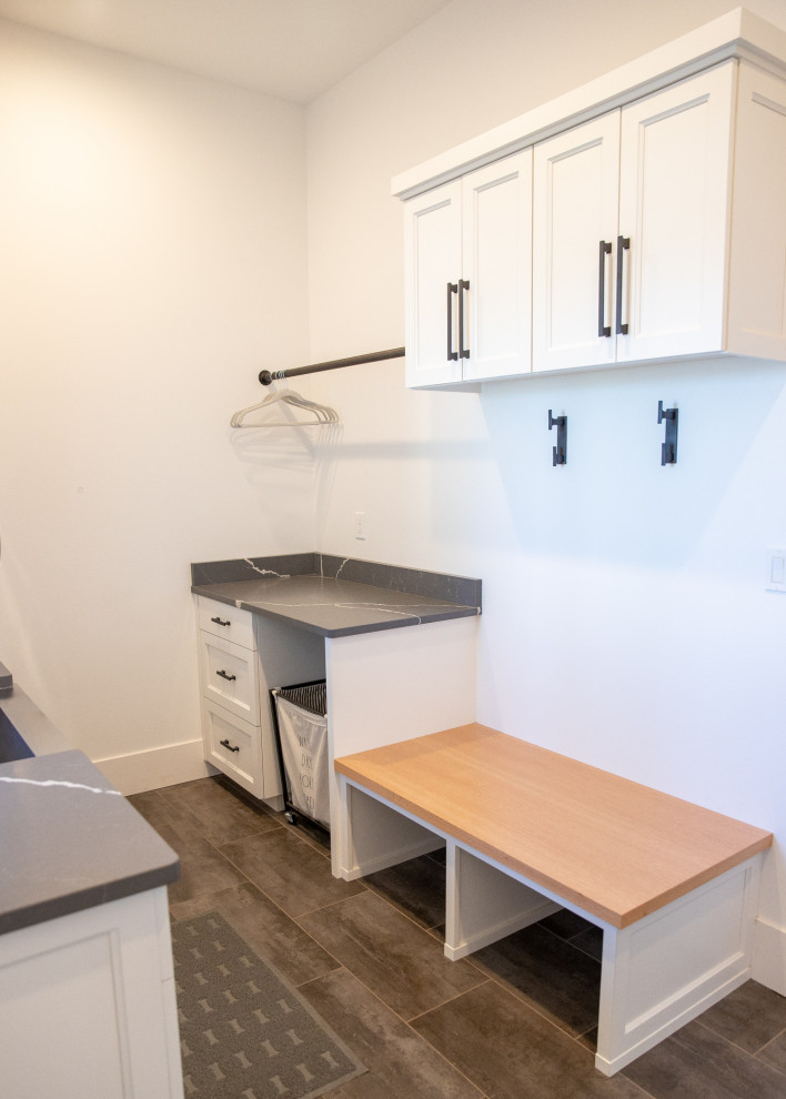 Photo of a small modern laundry room in Portland with a farmhouse sink, shaker cabinets, white cabinets, quartz benchtops, white walls, ceramic floors, a stacked washer and dryer, grey floor and grey benchtop.