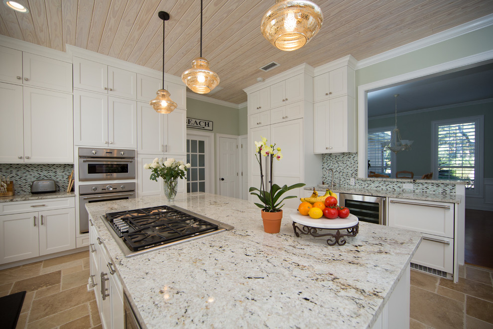 This is an example of a beach style kitchen in Jacksonville with a single-bowl sink, shaker cabinets, white cabinets, granite benchtops, green splashback, glass sheet splashback, panelled appliances and travertine floors.