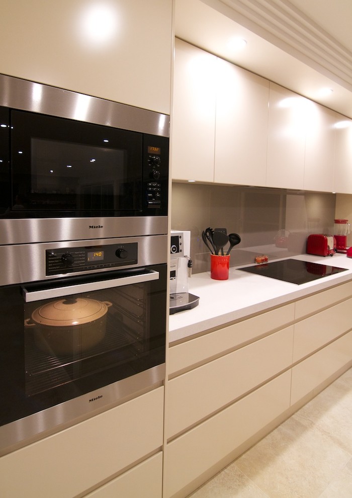Photo of a mid-sized contemporary galley open plan kitchen in Sydney with an undermount sink, flat-panel cabinets, beige cabinets, quartz benchtops, brown splashback, glass sheet splashback, stainless steel appliances, travertine floors, with island, beige floor and beige benchtop.